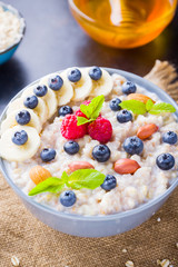 Oatmeal porridge with berries, fruits and honey on dark background. Oatmeal with raspberries, blueberries and almonds on burlap. Healthy breakfast