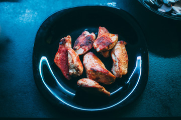 Fried chicken on a black plate in neon light.