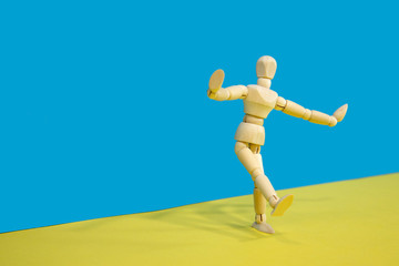 Wooden mannequin posing over yellow and blue background