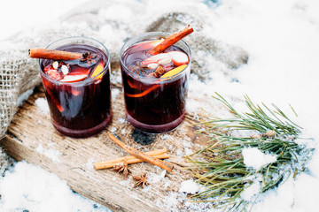 Mulled wine on a wooden board on a snowy table. Two glasses of hot wine with cinnamon and fresh...