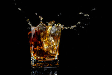  splash alcohol drink whiskey with ice with drops in a glass on a black background