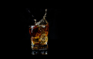  splash alcohol drink whiskey with ice with drops in a glass on a black background