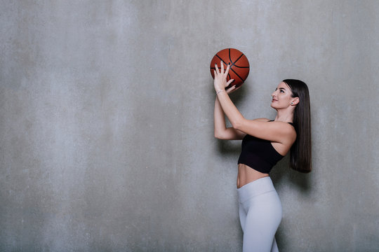 Portrait of a beautiful and girl with a basketball in studio. Sport concept isolated on grey background.