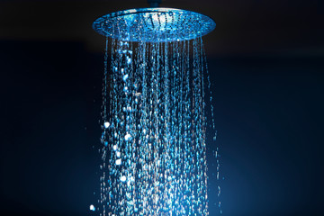 Water falling from the shower on a dark background with blue backlight in the aqua zone. - obrazy, fototapety, plakaty
