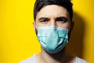 Close-up studio portrait of young man wearing medical flu mask on background of yellow color.