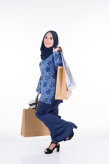 A beautiful and excited Muslim female model in a Asian traditional dress modern kurung carrying shopping bags isolated on white background. Eidul fitri fashion and festive preparation shopping concept