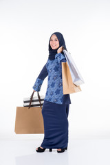 A beautiful and excited Muslim female model in a Asian traditional dress modern kurung carrying shopping bags isolated on white background. Eidul fitri fashion and festive preparation shopping concept