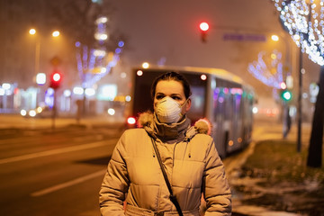 Young woman wearing mask to protect her from viruses, smog, exhaust fumes and other atmospheric pollutants in thick fog. Conceptual photo about health, ecology and air pollution.