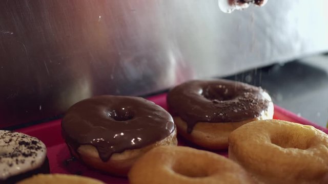 The baked donuts are being sprinkled by a topping. There are chocolate glaze and toppping on the donuts.