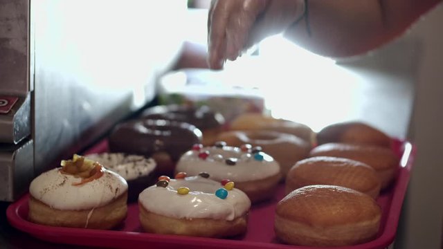 The baked donuts are being decorated by sweets. There are milky glaze and toppping on the donuts.