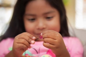 A child improving fine motor skills by using a pincer grip while holding string and beads.