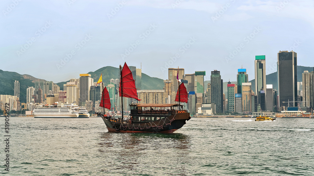 Wall mural junk boat at victoria harbor in hong kong at sundown. view from kowloon on hk island.