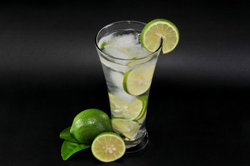 Glass of fresh lime with whole and sliced isolated on dark background