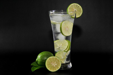 Glass of fresh lime with whole and sliced isolated on dark background