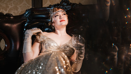 a girl in a gold dress with a diadem on her head, sitting on a leather armchair, looking towards...