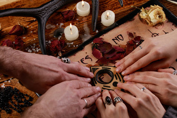 People conducting a seance using a Ouija Board, or Talking Spirit Board, with white candles. Shot...