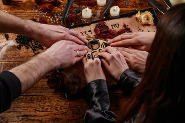 People conducting a seance using a Ouija Board, or Talking Spirit Board, with white candles. Shot from overhead.
