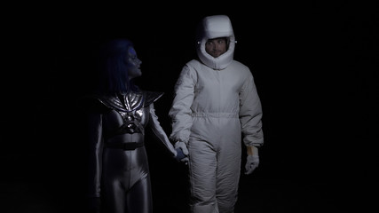 Fototapeta na wymiar Alien with blue skin goes with astronaut in the dark