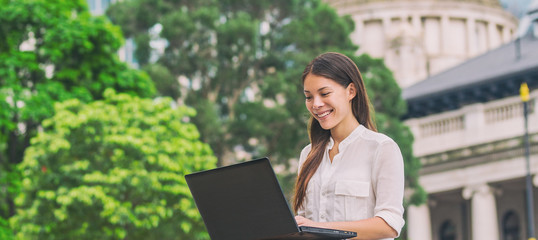 Asian business woman working on laptop computer outside in city park during lunch break, summer work lifestyle. Happy chinese biracial young lady.
