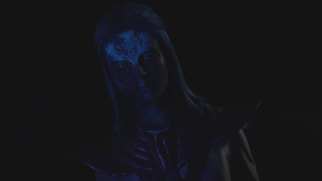 Alien with a glowing face looks at the camera in the dark