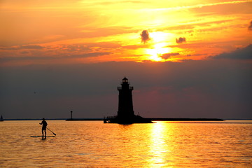 Silhouette of a light house and a man on a paddle board during sunset at Cape Henlopen State Park, Lewes, Delaware, U.S.A © Khairil