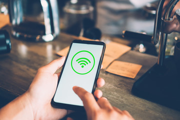 Woman hand using smartphone with wifi icon in cafe shop background.