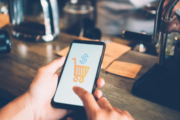 Women hand using smartphone do online business or shopping online in black friday with cart, dollar icons pop up in public area background.