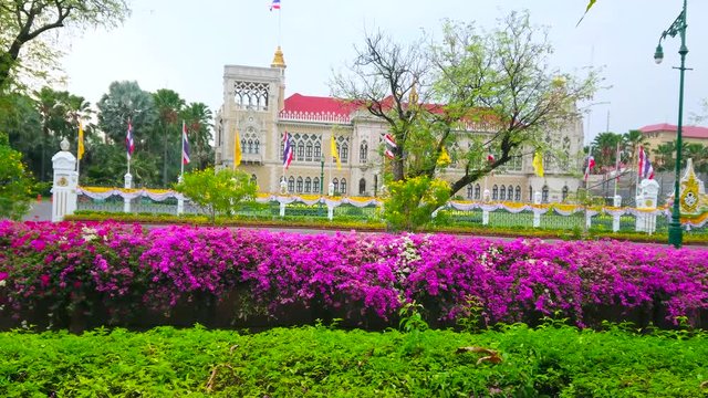 BANGKOK, THAILAND - MAY 13, 2019: The facade of Thai-Khu-Fah palace of Government House through the lush greenery and bougainvillea flowers around the Khlong Prem Prachakon canal, on May 13 in Bangkok