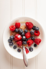 White bowl of cracked wheat cereal topped with blueberries, raspberries, and milk