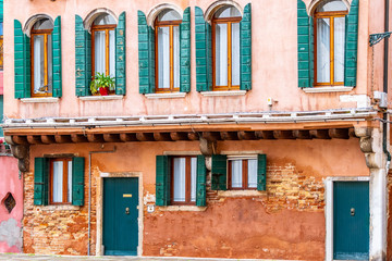 Fototapeta na wymiar Venice, Italy. European gothic design architecture. Typical traditional Venetian homes with wooden doors and knockers, large glass windows and shutters. Colorful residential small town neighborhood.