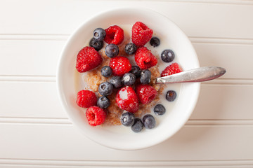 White bowl of cracked wheat cereal topped with blueberries, raspberries, and milk