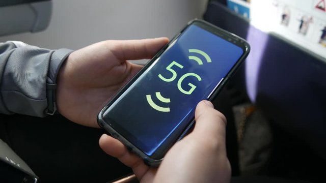 Holding a mobile phone receiving a 5G network signal inside an airplane.