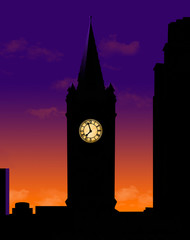 A clock tower is seen silhouetted at sunset with itâ€™s lighted clock face glowing in the dark.