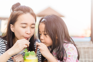 Happy laughing little girl and her beautiful young mother drinking fresh pineapple smoothie together in restaurant.Summer smoothie drink concept.