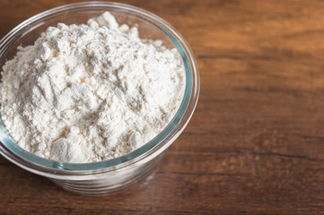 White flour in a glass bowl container on wood table surface.