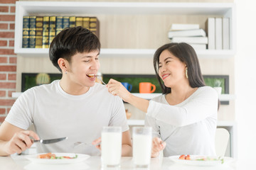 Obraz na płótnie Canvas Happy Married lover couple eating breakfast at home.Lover couple wear white t shirt and holding fork and knife ready for breakfast.