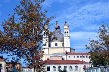 part of one of the Venetian churches against the bright blue sky, slightly obscured by a tree in the foreground