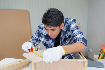 Young asian carpenter with safety glasses measuring on wooden job with tape measure - Handyman and...