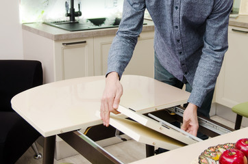 man lays out a sliding glossy dining table on which stands a plate with artificial fruit