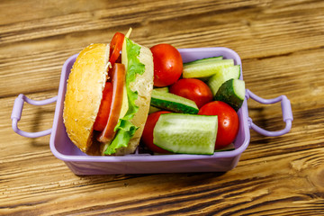 Lunch box with burgers and fresh vegetables on a wooden table