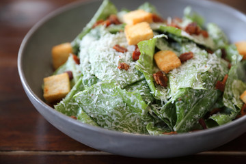 Caesar salad with crispy bread and bacon close up on wood background