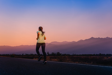Woman running on road with a view of mountains in the morning.