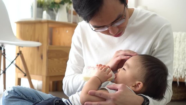 Asian family of young father feeding a baby boy from milk bottle at home