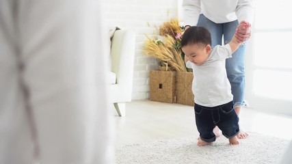 Asian baby boy toddler taking first steps. Family of father and mother encouraging their son learning to walk at home