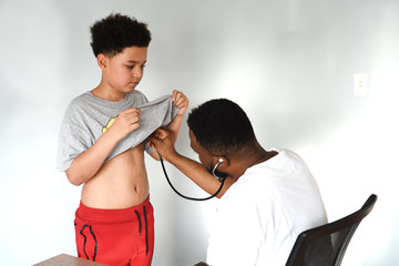 An african american doctor with his mixed preteen male. A cute black paediatrician examining his young mixed preteen boy patient with a stethoscope.