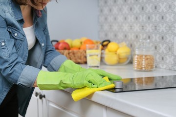 Woman hands in gloves washing and cleaning electric hob in kitchen