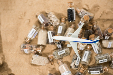 Glass test-tube with sand of different summer vacation countries. Located in sand with small airplane.