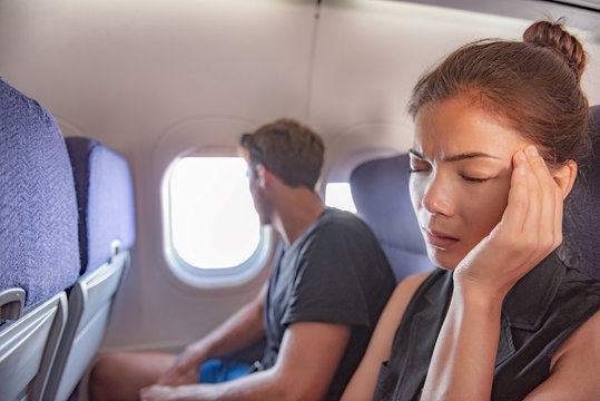 Sick woman in airplane fear of flying inside plane cabin with headache. Asian passenger on travel feeling sick with stress anxiety migraine. Couple tourists.