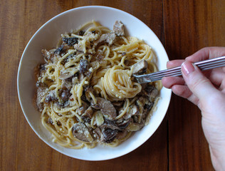 Mushroom white pasta topped with parmesan on a white plate and on top of a wooden table. 
