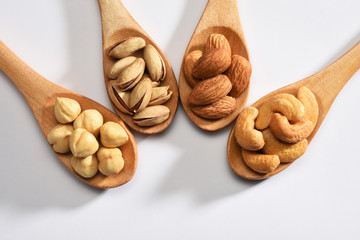Hazelnuts, almonds, pistachios and cashews in the wooden spoons on white background	